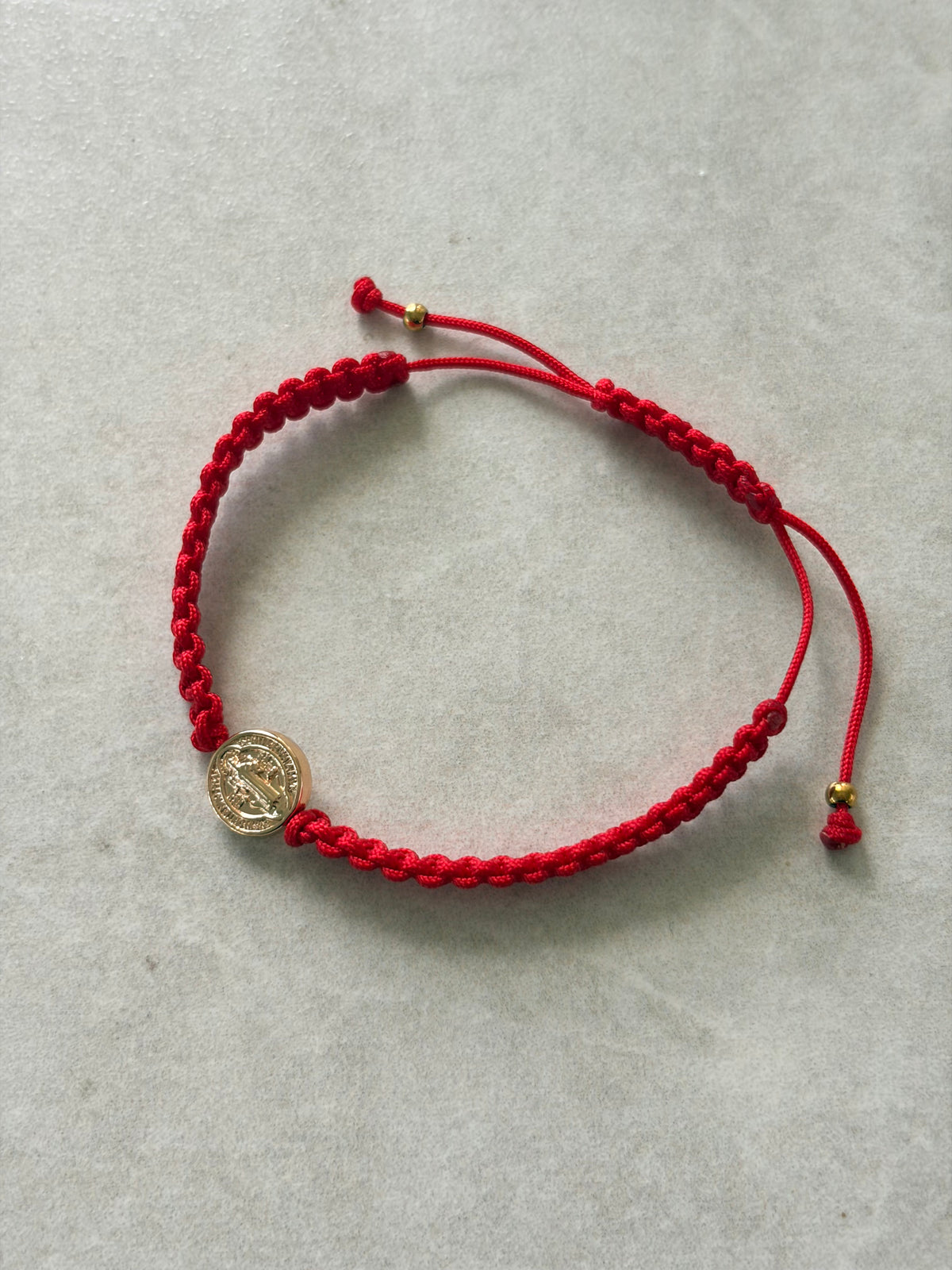 Pulsera San Benito dorada en hilo rojo